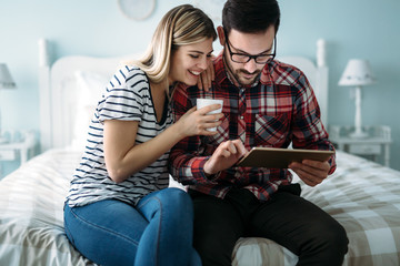 Young happy couple using tablet in bedroom