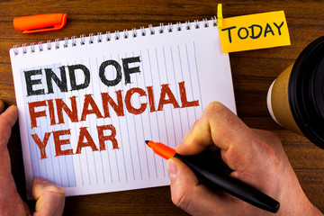 Text sign showing End Of Financial Year. Conceptual photo Taxes time accounting June database cost Sheets written by Man Notepad holding Marker Wooden background Today Cup and Clip.