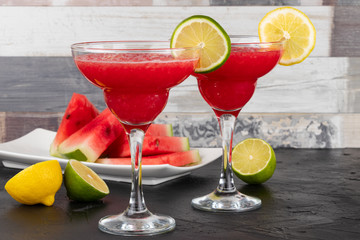 Two watermelon smoothies with slices of watermelon, lemon and lime