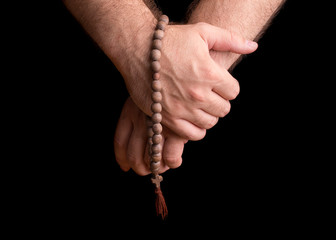 Hands of a male priest with a wooden rosary. Priest with a rosary in his hand on a dark background.