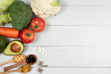 Vegetables and vitamins placed on a white wooden table.