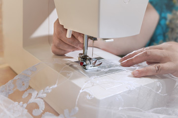 Seamstress sews a white curtain on a sewing machine.