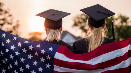 Two college graduates in gowns and caps with the American flag