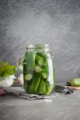 Pickling and fermentation cucumber in glass jar with dill and garlic on dark grey concrete tabletop.