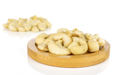 Lot of whole unsalted beige cashew on round bamboo coaster isolated on white background