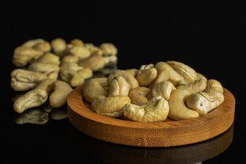 Lot of whole unsalted beige cashew on round bamboo coaster isolated on black glass