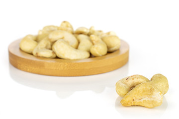 Lot of whole unsalted beige cashew on round bamboo coaster isolated on white background
