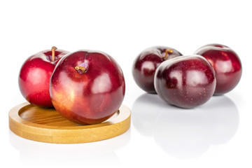 Group of five whole ripe red round plum on round bamboo coaster isolated on white background