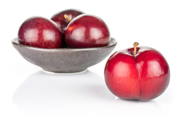Group of four whole ripe red round plum in dark ceramic bowl isolated on white background