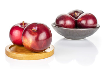 Group of five whole ripe red round plum in dark ceramic bowl on round bamboo coaster isolated on white background