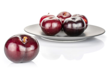 Group of six whole ripe red round plum on gray ceramic plate isolated on white background