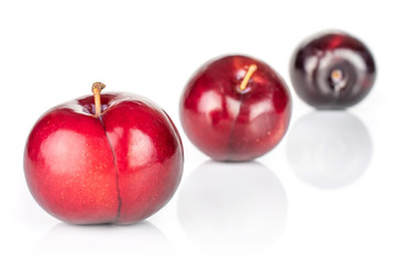 Group of three whole ripe red round plum placed diagonally in line isolated on white background