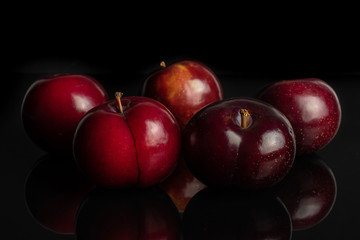 Group of five whole ripe red round plum arranged symmetrically isolated on black glass