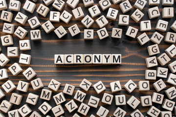 acronym - word from wooden blocks with letters, use of acronyms in the modern world abbreviation concept, random letters around, top view on wooden background - obrazy, fototapety, plakaty