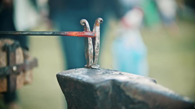 Blacksmith working with an iron details in his workshop - bending the heated piece of metal in semicircle