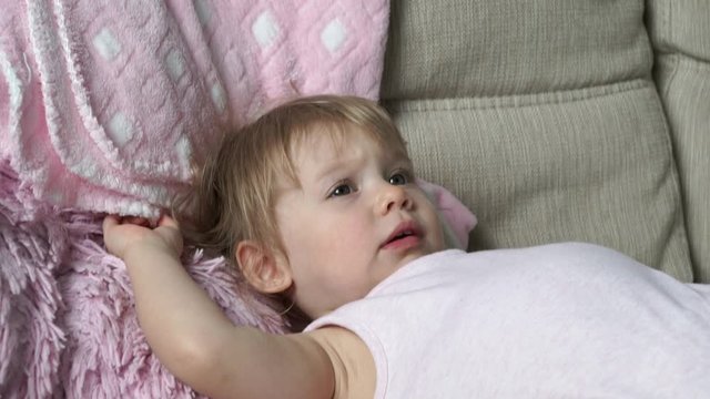 Portrait of little cute 2 year old baby girl in pink clothes lies on bed, plays with her feet and smiles