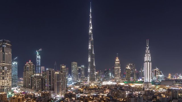 Dubai Downtown skyline all night timelapse with Burj Khalifa and other towers paniramic view from the top in Dubai, United Arab Emirates. Lights swithcing off. Traffic on circle road and fountains.