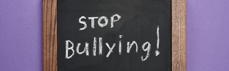 panoramic shot of chalkboard in wooden frame with stop bullying lettering on purple background