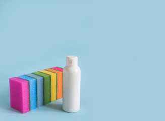 on a blue background are seven rectangular washcloths in a row of sponges for dishes for cleaning the purity of all the colors of the rainbow and next to it is a white plastic bottle with a detergent