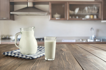 Fototapeta na wymiar Glass of fresh milk and jug on wooden tabletop with blur kitchen as background. Space for text or display product.
