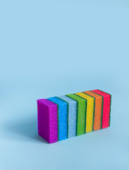 on a blue background are rectangular washcloths in a row of seven sponges for dishes to clean all rainbow colors