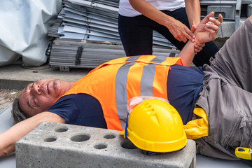 Cropped image of a paramedic's hands checking the pulse rate of a lying down construction worker injured at work