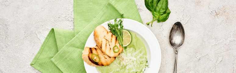panoramic shot of delicious creamy green vegetable soup with croutons served with napkin and spoon