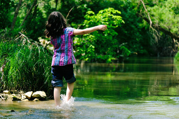 Young girl in nature during summer, walking through water in creek having fun.