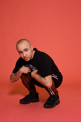 Studio shot of a young tattoed bald man posing against a pink background. 90s style.