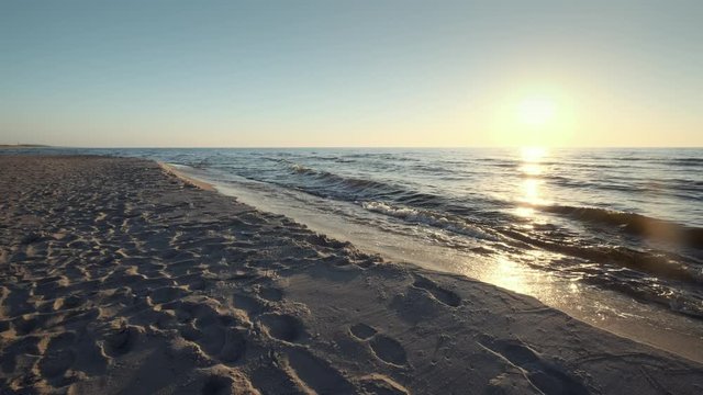 Sun low above horizon, sandy beach of Baltic sea at Curonian spit, soft waves