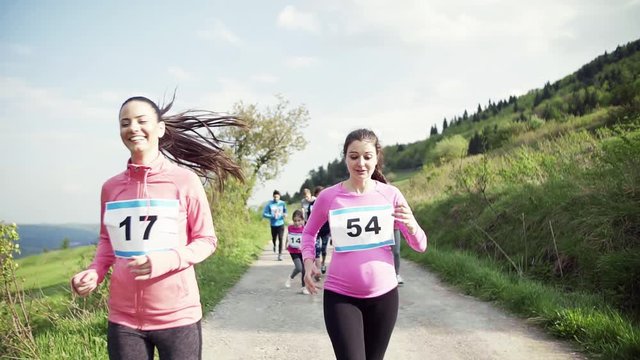 Pregnant woman with group of people running a race competition in nature.