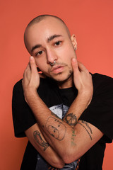 Studio shot of a young tattoed bald man posing against a pink background. 90s style.