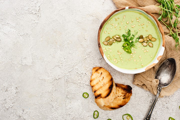 top view of tasty green creamy soup with croutons and sprouts on textured grey background with rustic cloth