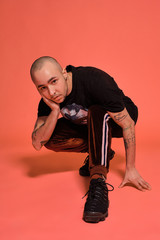 Studio shot of a young tattoed bald man posing against a pink background. 90s style.