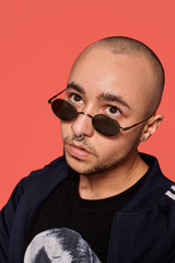 Fototapeta premium Studio shot of a young tattoed bald man posing against a pink background. 90s style.