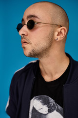 Studio shot of a young tattoed bald man posing against a blue background. 90s style.