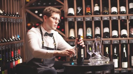 Elegant young sommelier with bow tie uncorking bottle of wine in wine boutique. Wine tasting social event.