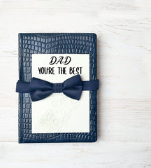 Happy Father's Day holiday concept. blue leather bound journal and bow tie. Greeting card with text "Dad you're the best". idea and symbol for gift dad, men, brutal style. holiday background. top view