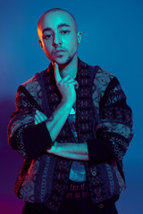 Studio shot of a young tattoed bald man posing against a colorful background. 90s style.