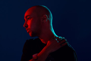 Studio shot of a young tattoed bald man posing against a blue background. 90s style.