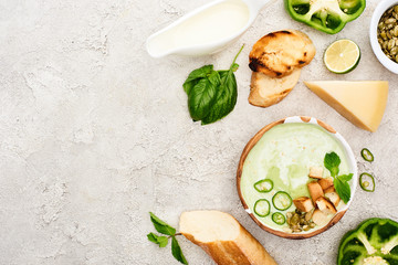 top view of tasty green creamy soup with croutons and greenery on textured grey background