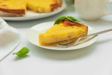 Sliced upside down pineapple cake decorated green leaves with cup of tea on white table. Summer tropical dessert. Front view. Copy space