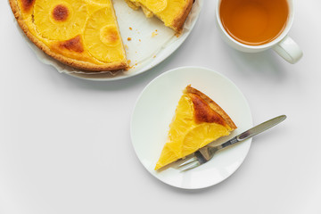 Sliced upside down pineapple cake with cup of tea on white table. Summer tropical dessert. Top view. Copy space