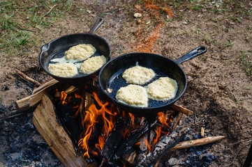 Potato pancakes fried in hot oil on a nature background. Preparing food on campfire in wild camping. Ukrainian cuisine