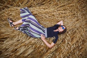 Beautiful young woman lies in a field of wheat dressed in a stylish dress and glasses