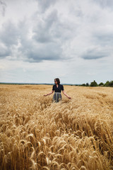 Beautiful young woman in a field of wheat dressed in a stylish dress and glasses