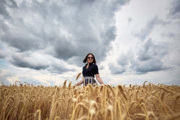 Beautiful woman in a field of wheat dressed in a stylish dress and glasses