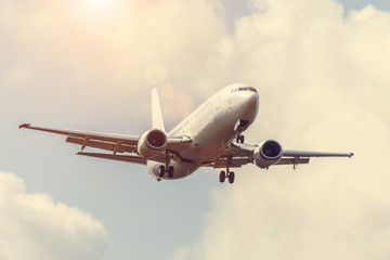 Sky with clouds and sun with a warm shade, reflected glare light, and passenger airplane landing approach airport.