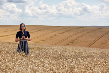 Beautiful young woman in a field of wheat dressed in a stylish dress and glasses. Surrounded by beautiful clouds