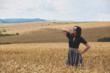 Beautiful woman in a field of wheat dressed in a stylish dress and glasses. Surrounded by beautiful clouds
